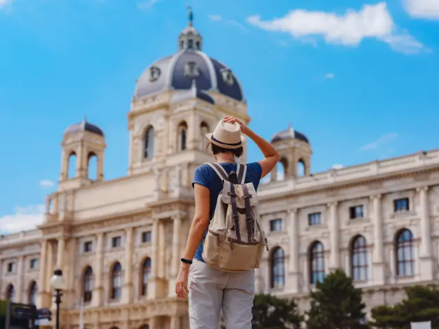 Turista de chapéu e mochila diante de um edifício histórico europeu durante viagem ao exterior